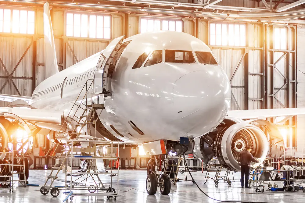 A large commercial airplane undergoing maintenance in a bright, spacious hangar.